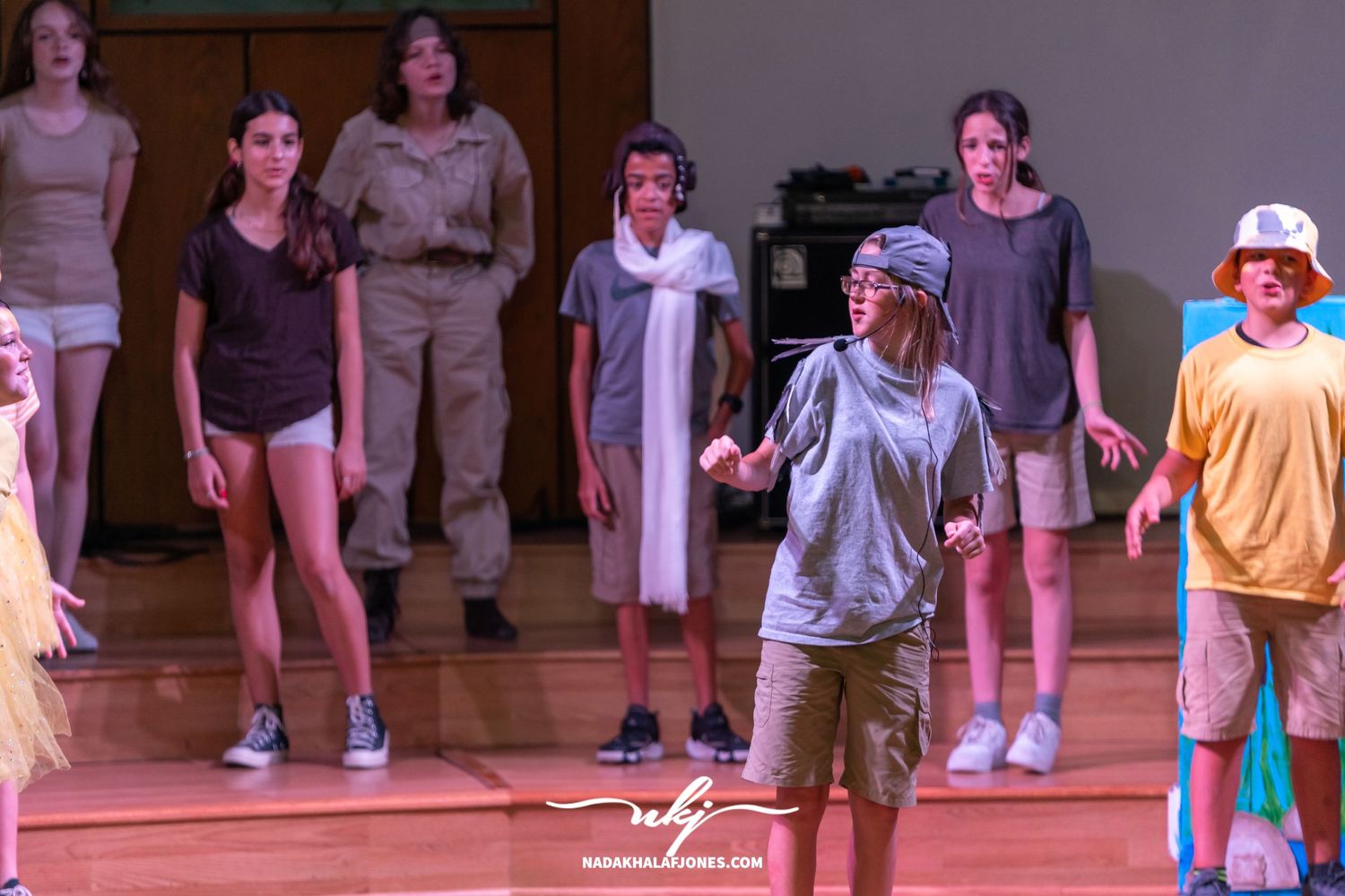 Theater cast members in casual costumes perform together during a stage production.