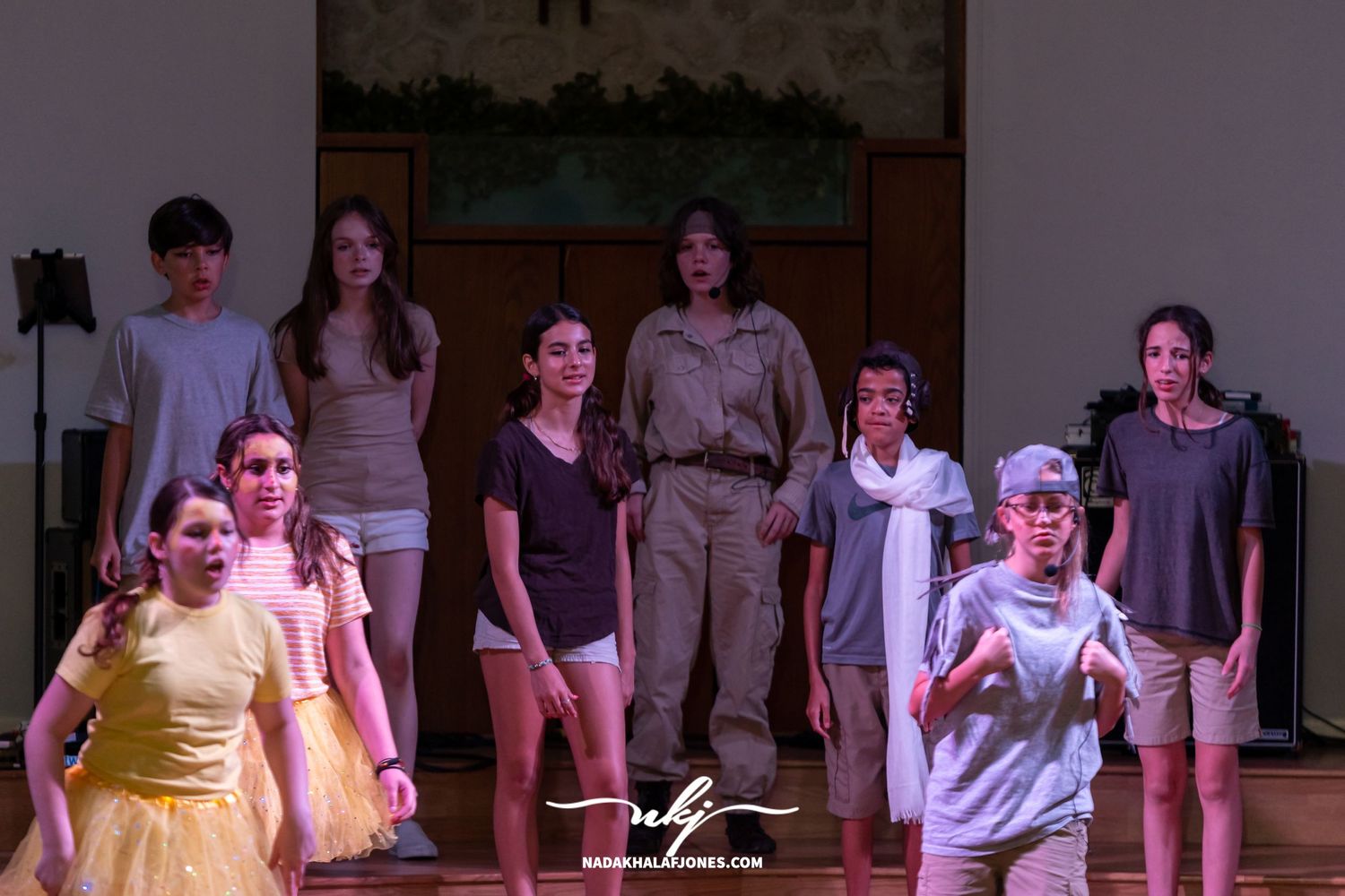 Cast members act out a scene on stage with dramatic lighting and minimal set design.