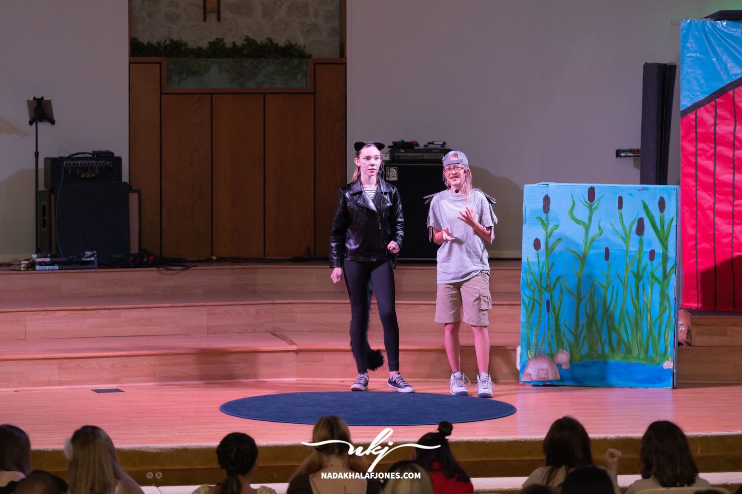 Stage actors perform in front of painted backdrops during a theatrical production.