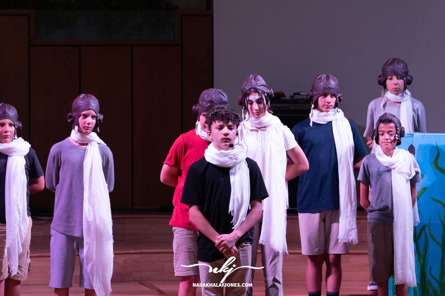 Stage performance showing cast members in white costumes lined up during dramatic scene.