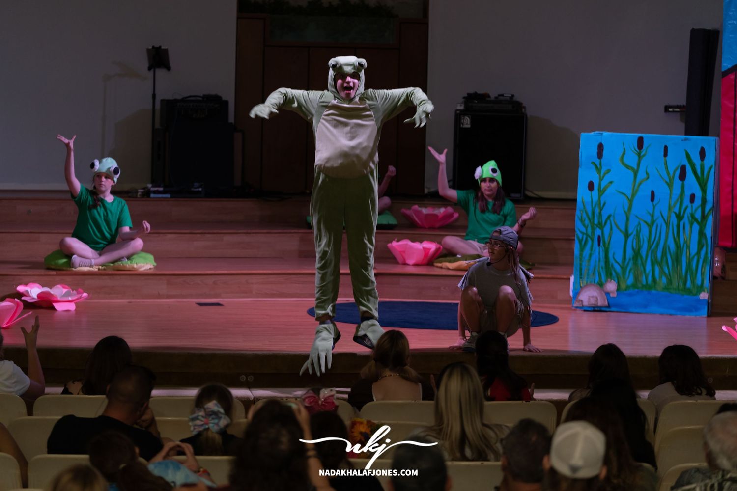 Stage performers in artistic poses during theatrical production with colored stage lighting.