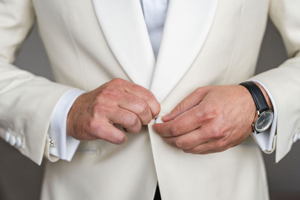 Close up of hands adjusting buttons on a white formal suit jacket.