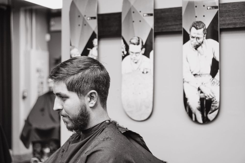 A man in a barber’s chair looks down while he gets his hair cut