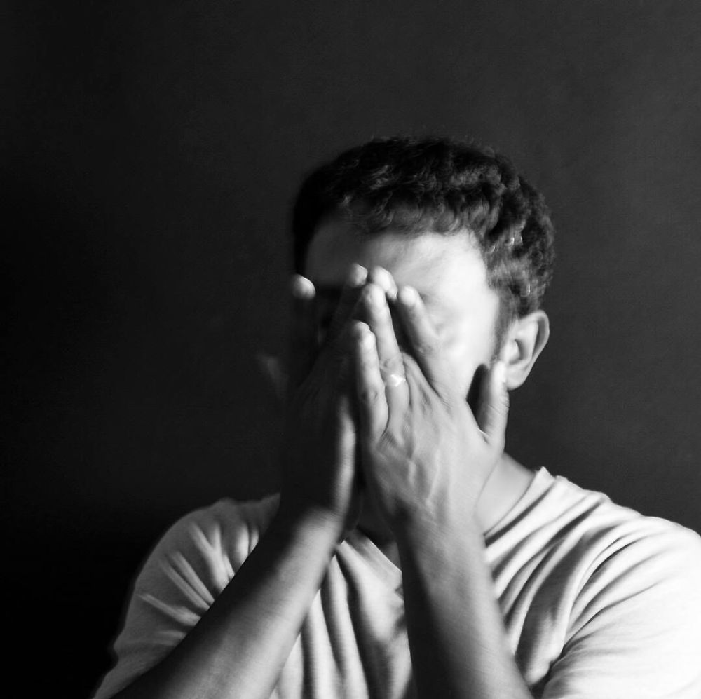 A man with short dark hair and olive complexion holds his hands against his face