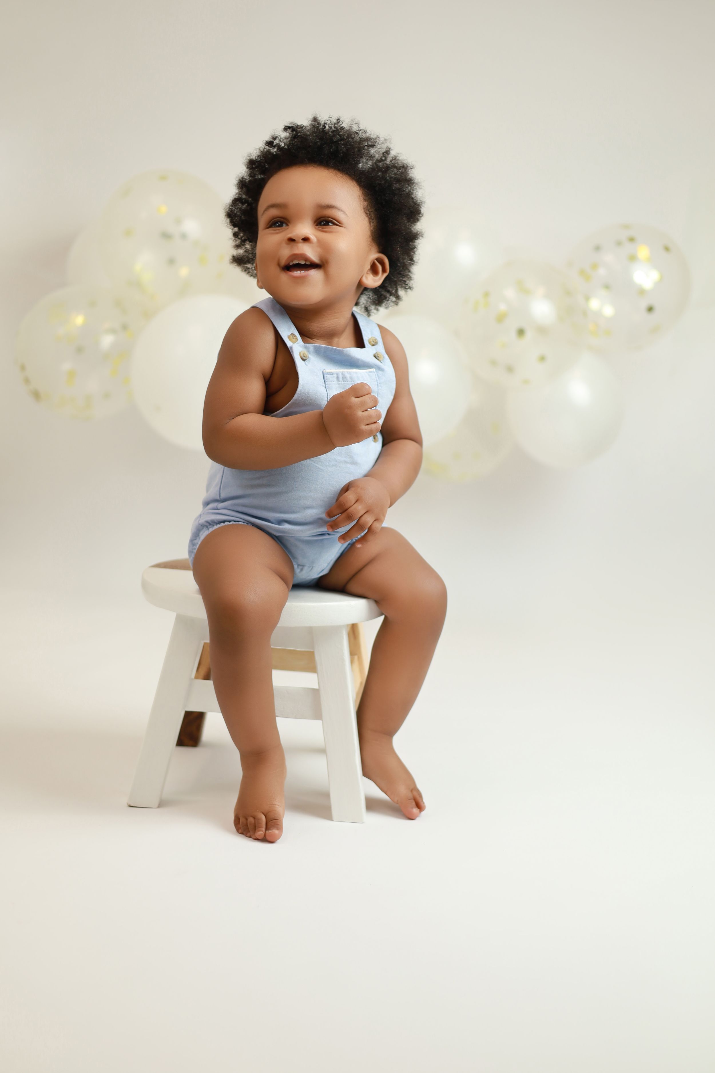First birthday cake smash session with a happy toddler enjoying their cake surrounded by balloons.