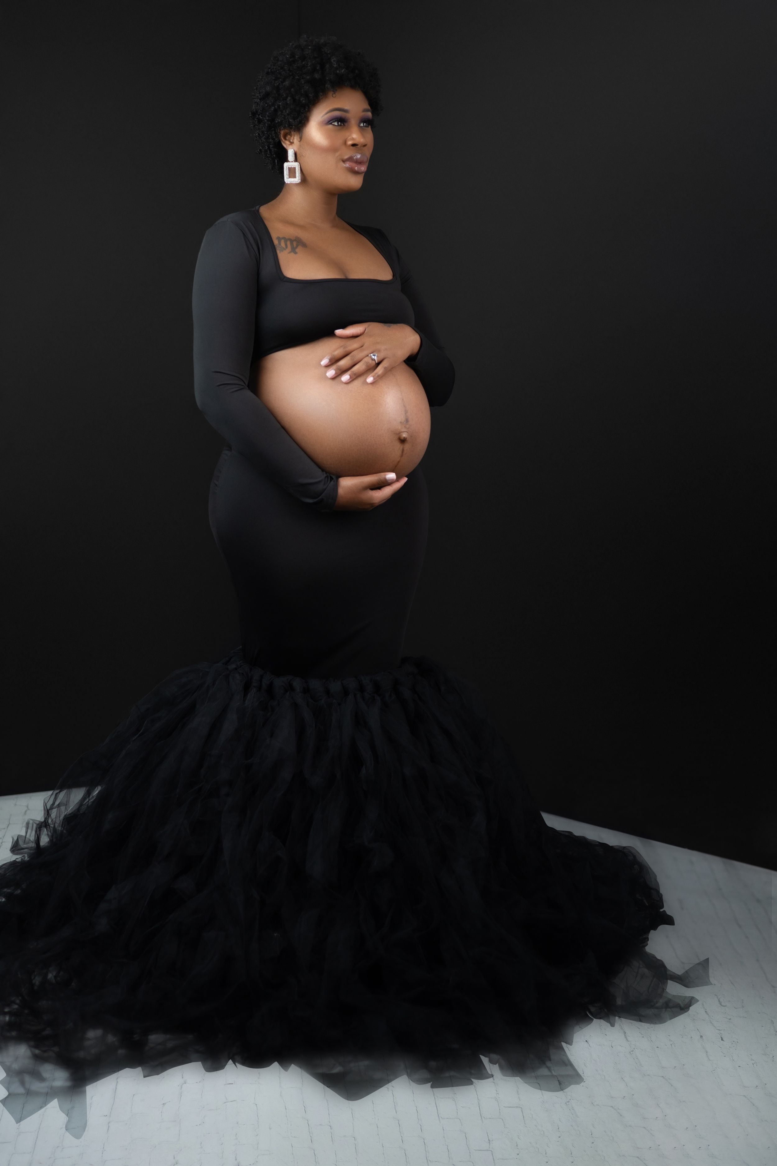 Close-up of a glowing mom-to-be smiling while holding her bump in a cozy studio setting.