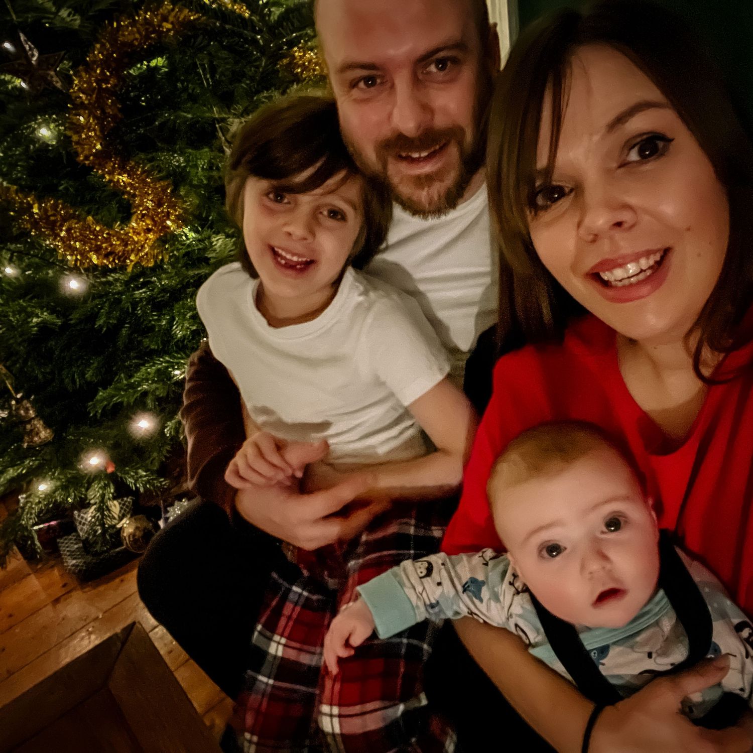 A cozy family Christmas photo in front of a decorated tree with twinkling lights.