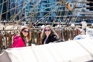 Two people enjoying a sunny day on a boat deck surrounded by sailing equipment and rigging.