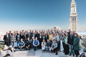 Large group photo of business professionals gathered on rooftop with historic clock tower visible.