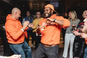Two people in bright orange hoodies celebrating energetically at an indoor social gathering.