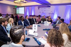 Business professionals gather around a conference table for a meeting in a blue-lit room.