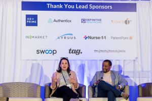 Speakers on stage with sponsor wall displaying tech company logos at a professional event.