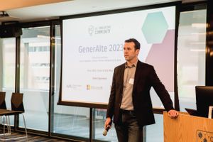 Business presenter speaking at GenerateAI 2023 conference with projection screen visible.
