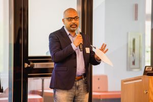 Speaker presenting in business attire at corporate conference with microphone.