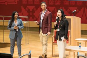 Speakers present on stage at Harvard Business School event with red backdrop.