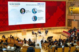 Business conference session in an auditorium with presentation slides and panel discussion setup.
