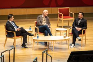 Panel discussion with three speakers seated on stage with wooden chairs and table.