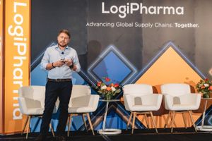Speaker presenting at LogiPharma conference with branded backdrop.