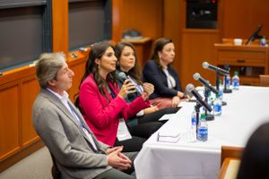 Business panel discussion with speakers seated at table with microphones in conference room.