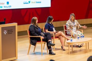 Speakers engage in discussion during MBA Brasil conference with red stage backdrop.