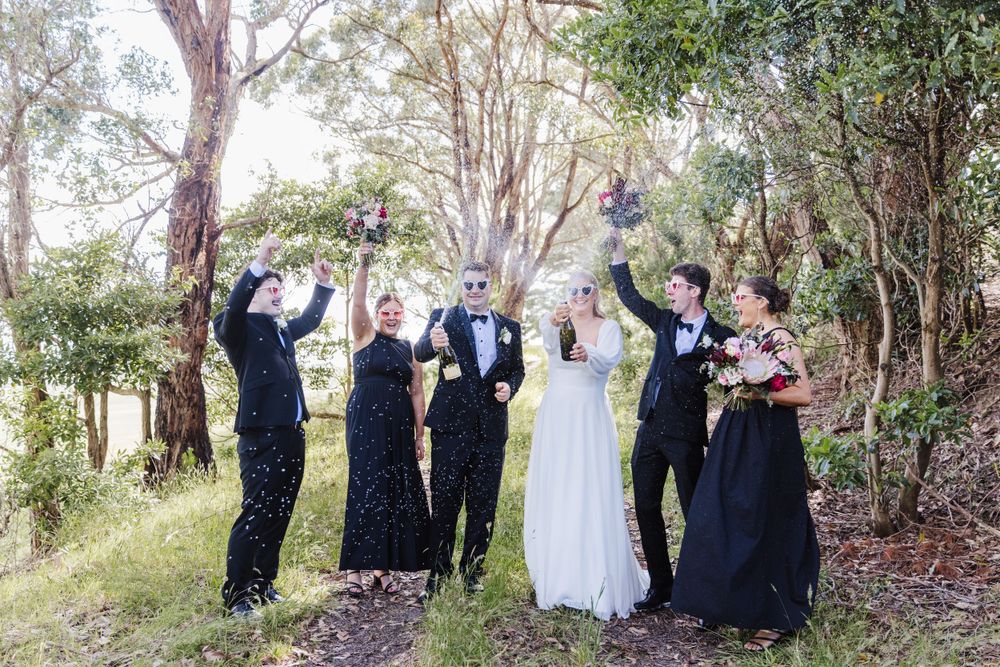 Wedding party celebrates joyfully under trees in an outdoor setting.