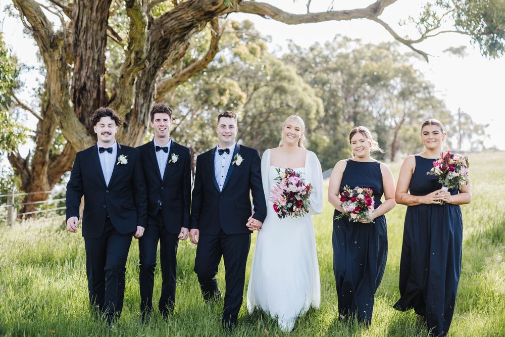 Wedding party stands in formal attire beneath towering eucalyptus trees on a grassy hillside.