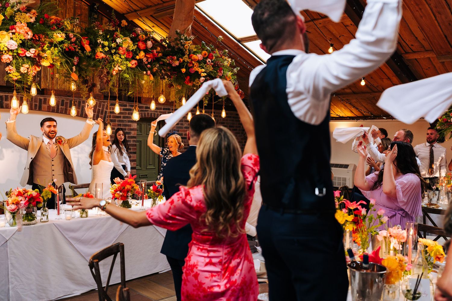 Bride and groom make grand entrance into floral-decorated wedding reception as guests cheer and wave napkins at Owen House Wedding Barn.