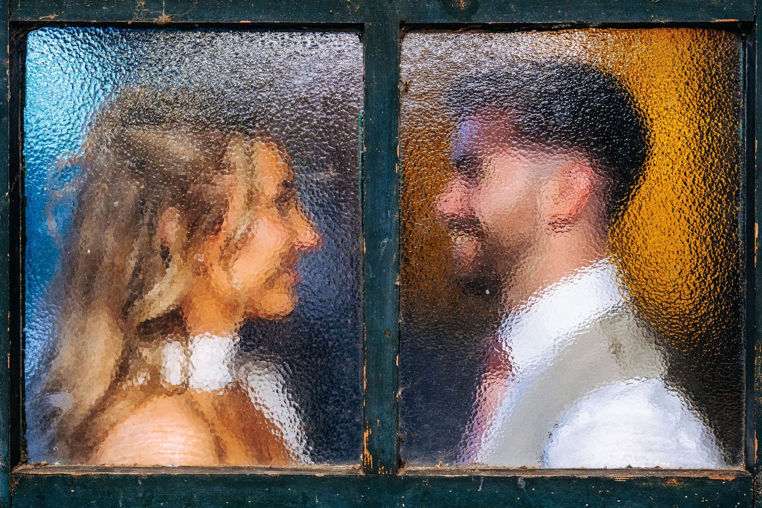 Abstract wedding portrait of bride and groom facing each other viewed through vintage textured glass window panes at Owen House Wedding Barn