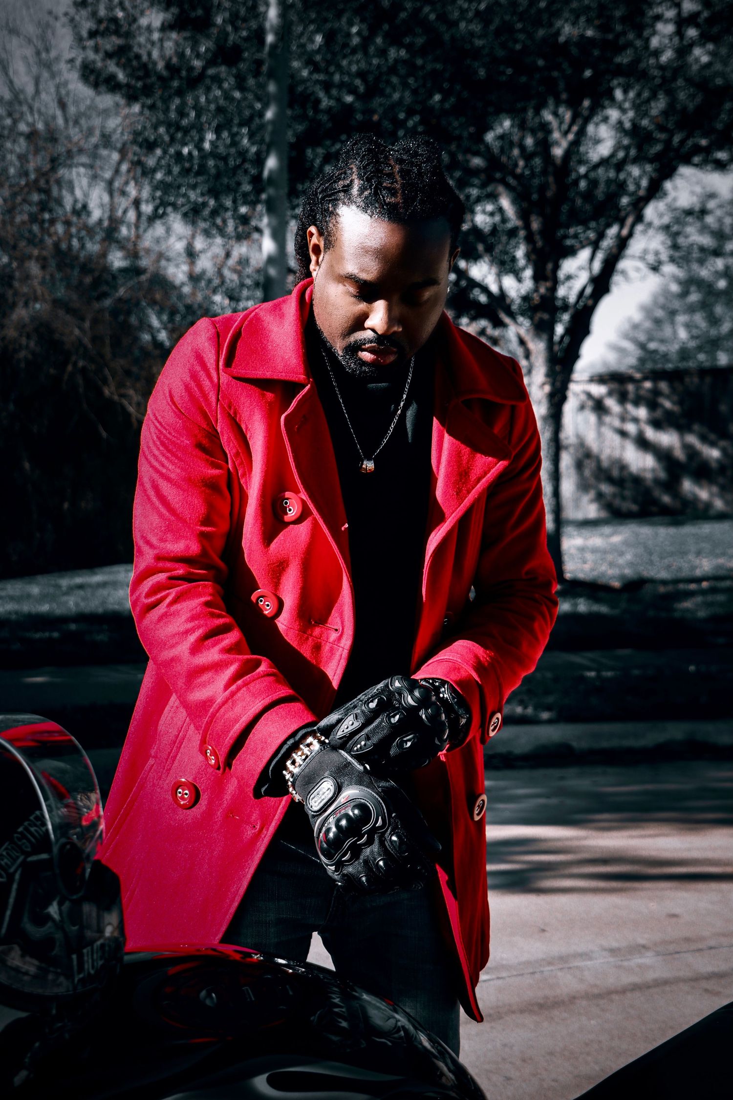 Dramatic portrait of person in red coat with motorcycle in moody outdoor setting.