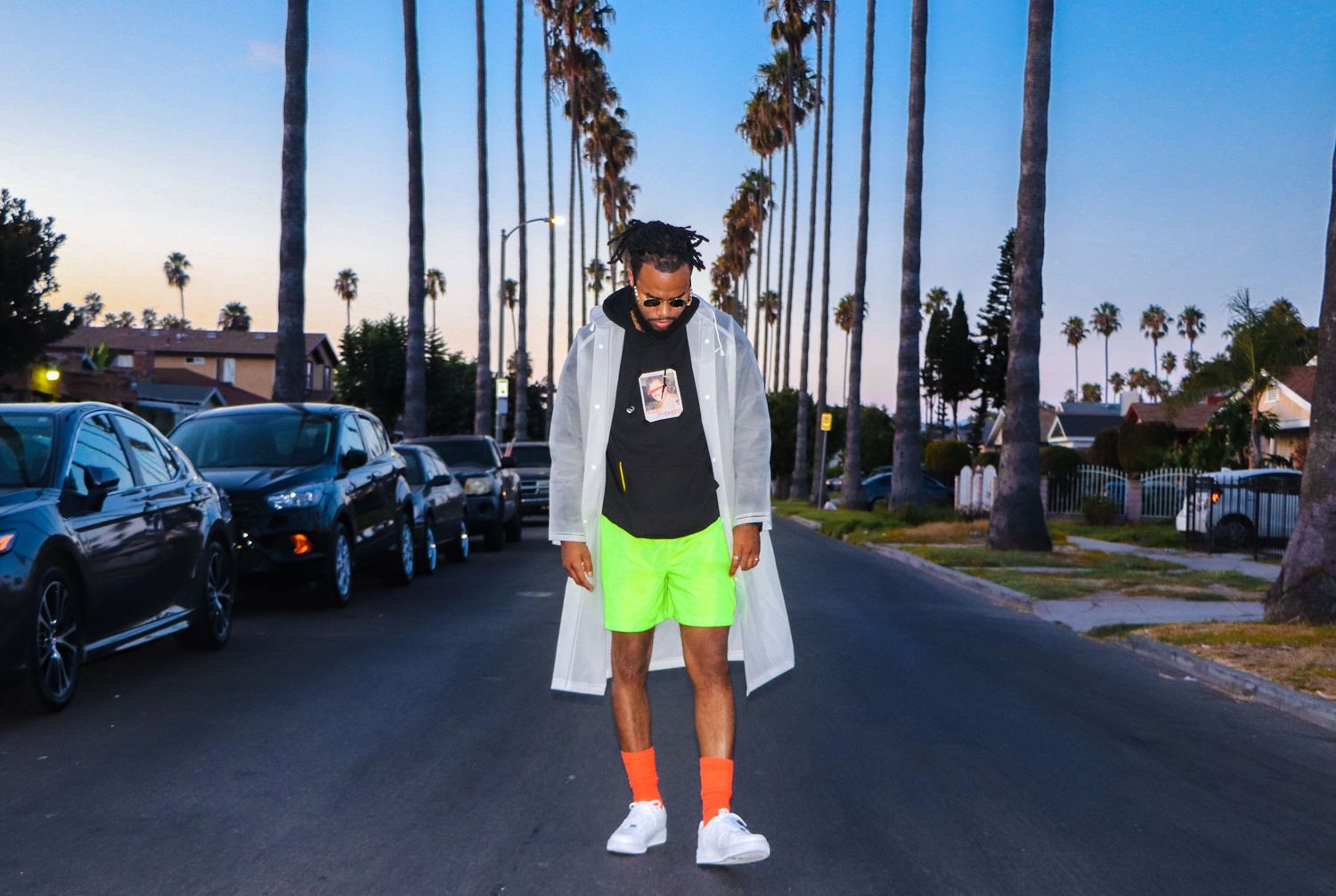 Street style fashion shot with neon shorts and white coat against palm tree backdrop.