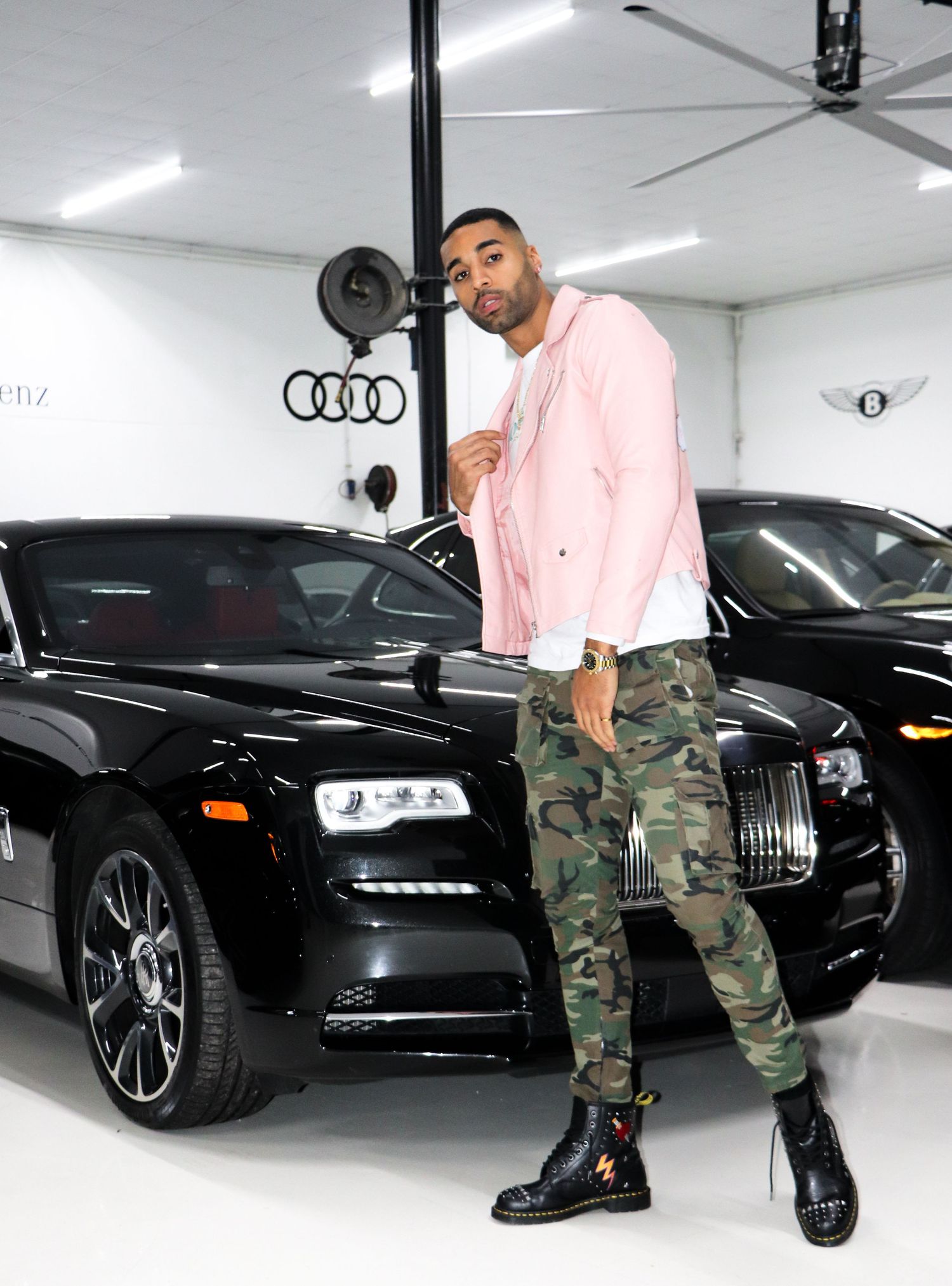 Stylish photo of pink jacket and camo pants in luxury car showroom with Rolls Royce.