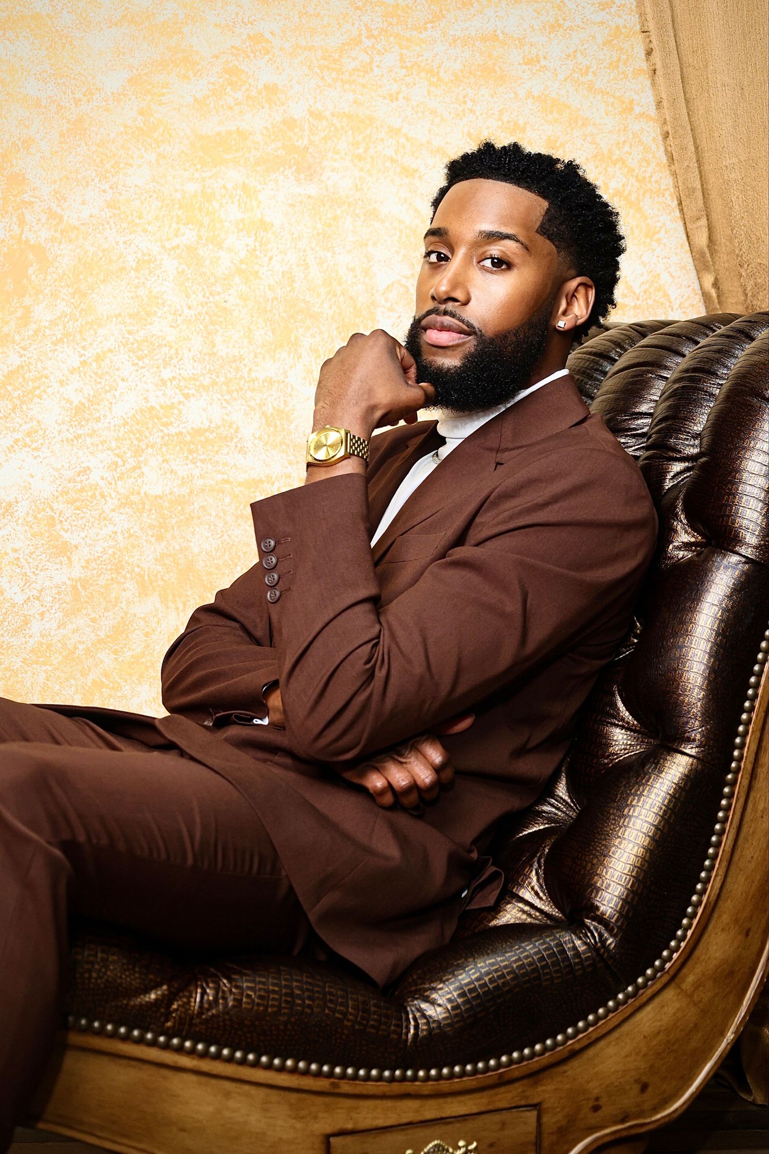 Elegant portrait of model in brown suit reclining on leather chair.