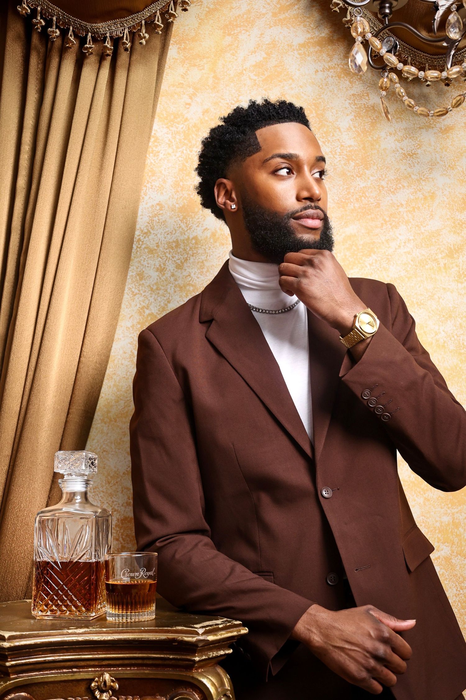 Fashion portrait of model in brown suit with turtleneck next to whiskey decanter.