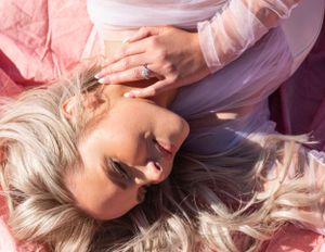Overhead view of blonde woman lying on pink fabric wearing a sparkling ring.