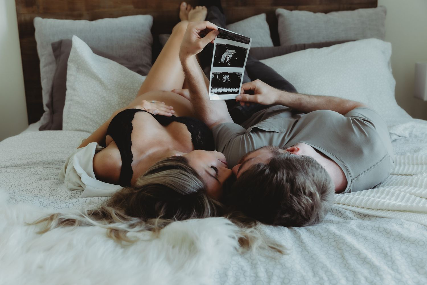 Couple laying in bed during maternity shoot watching pictures from the pregnancy scan in Dubai.