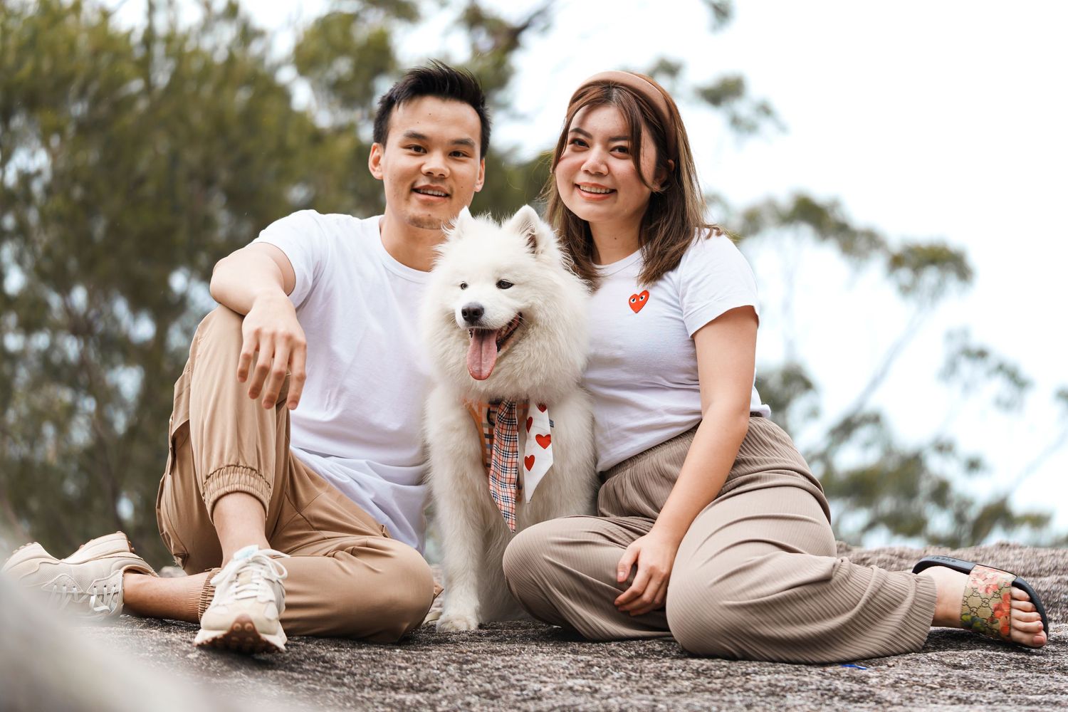 White Samoyed dog sitting with companions outdoors in casual attire.