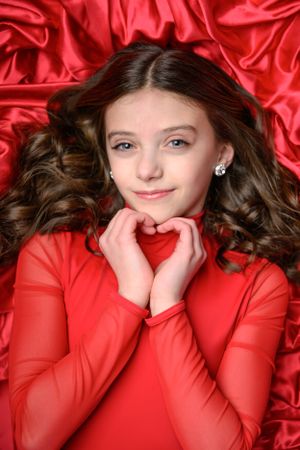 Portrait of person in red top lying on silk fabric backdrop.