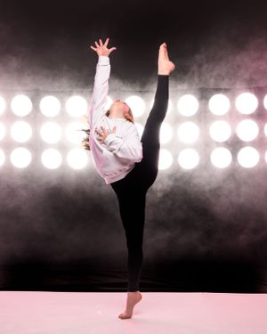 Modern dancer executes high kicks and graceful movements in front of bright stage lights.