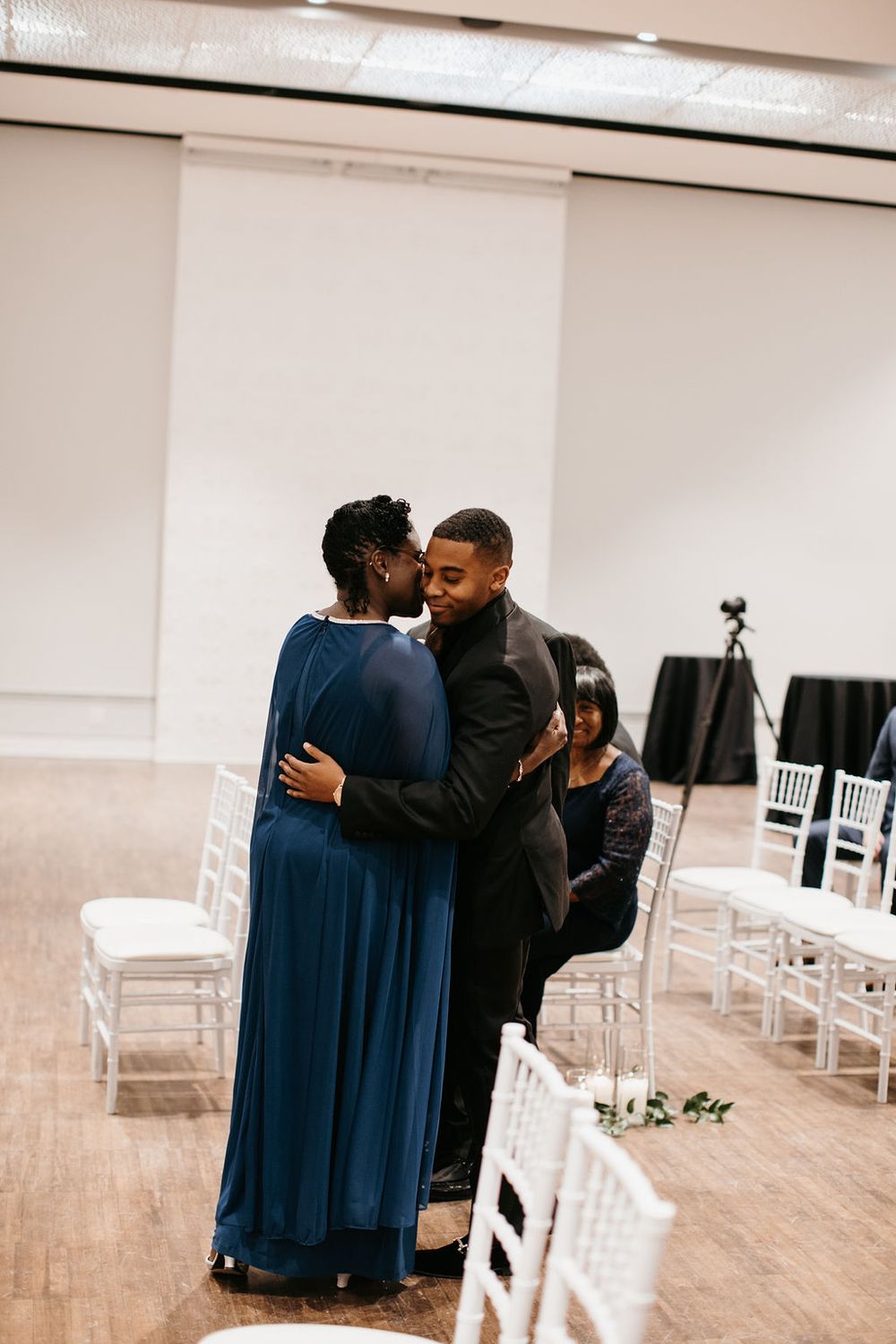 Groom shares a warm embrace with his mother in a white Chiavari chair wedding ceremony venue.