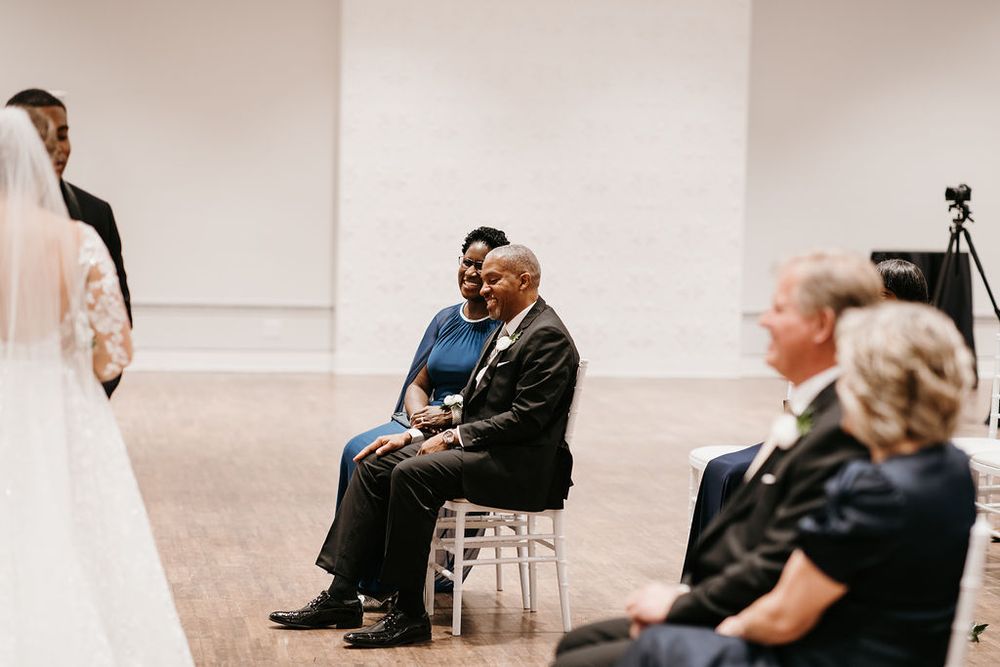 Seated wedding guests smile warmly while watching the ceremony unfold in a bright modern venue.