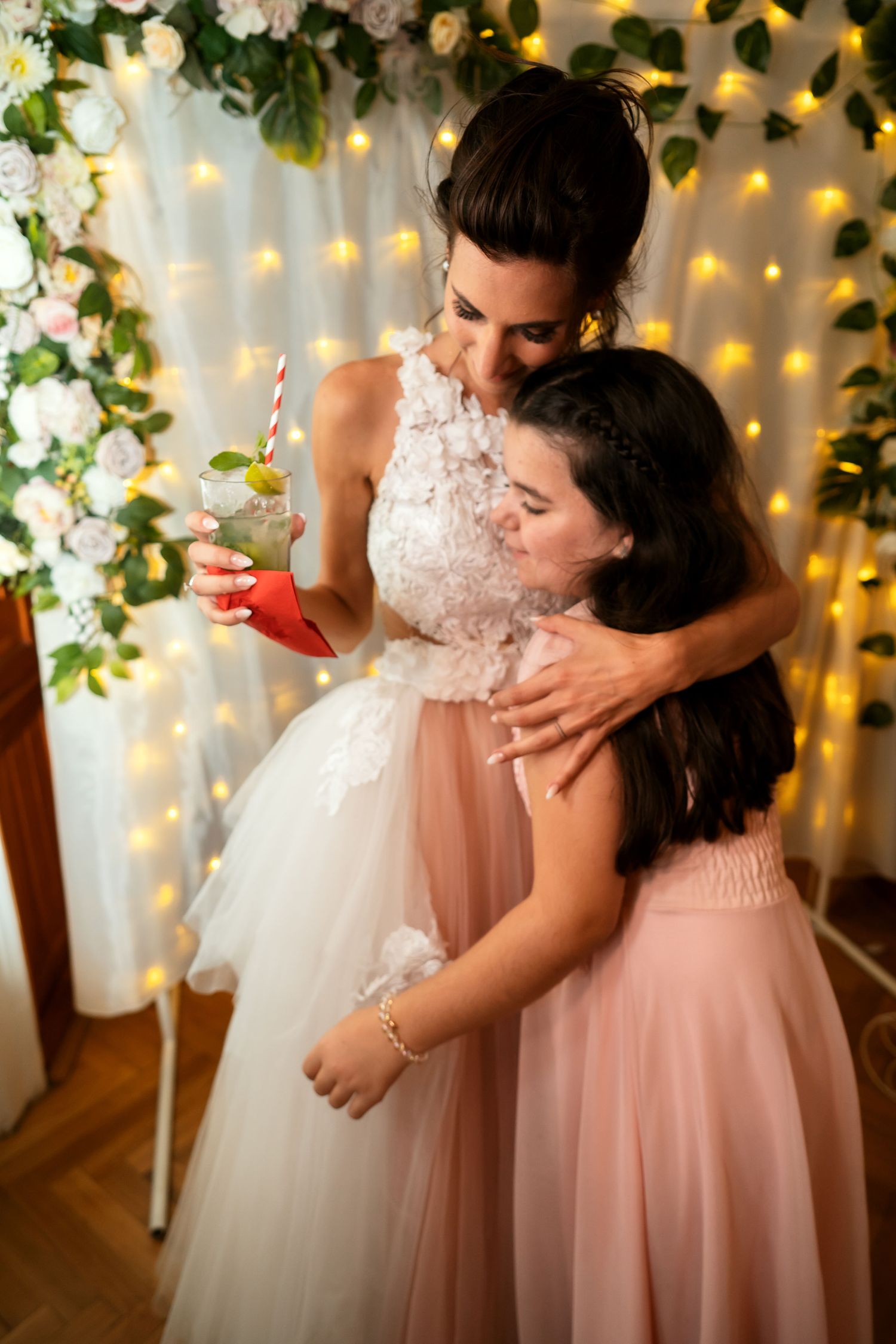 Tender moment under floral arch and string lights at wedding reception.