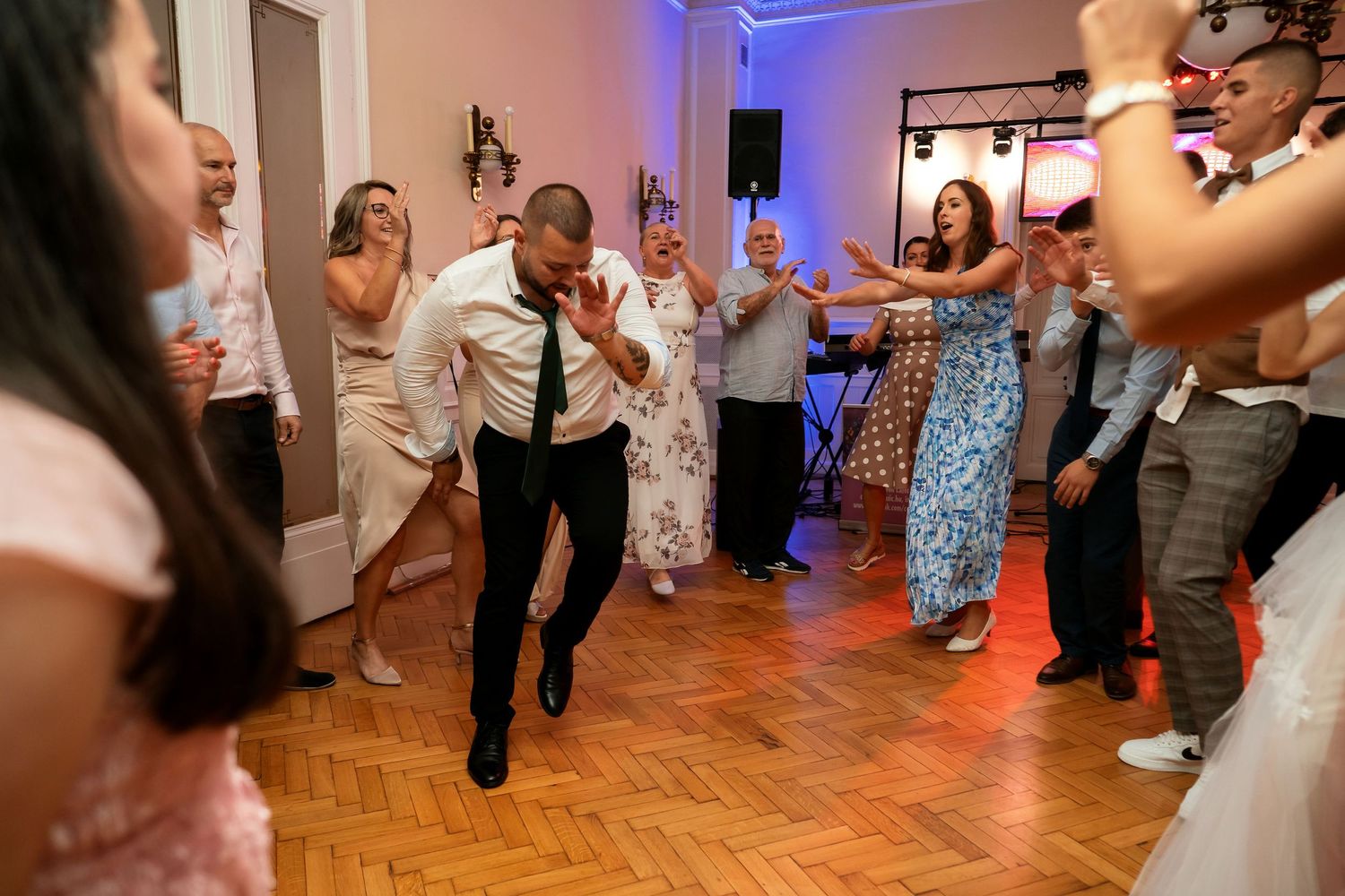 Energetic dancing at wedding reception with colorful mood lighting on parquet floor.
