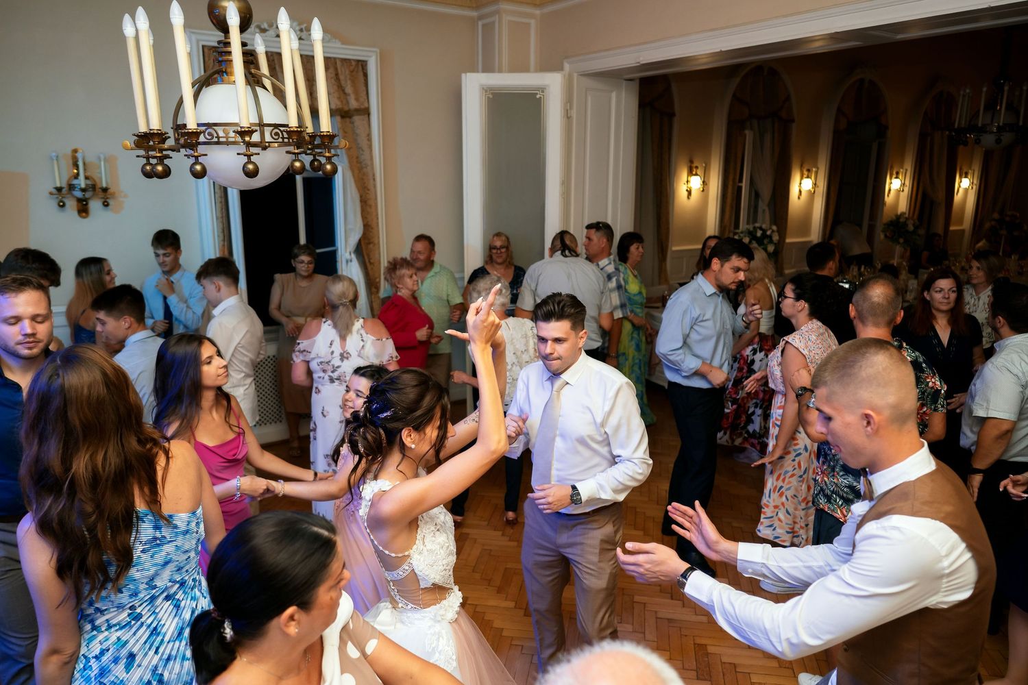 Lively wedding reception dance floor with guests enjoying themselves under chandeliers.