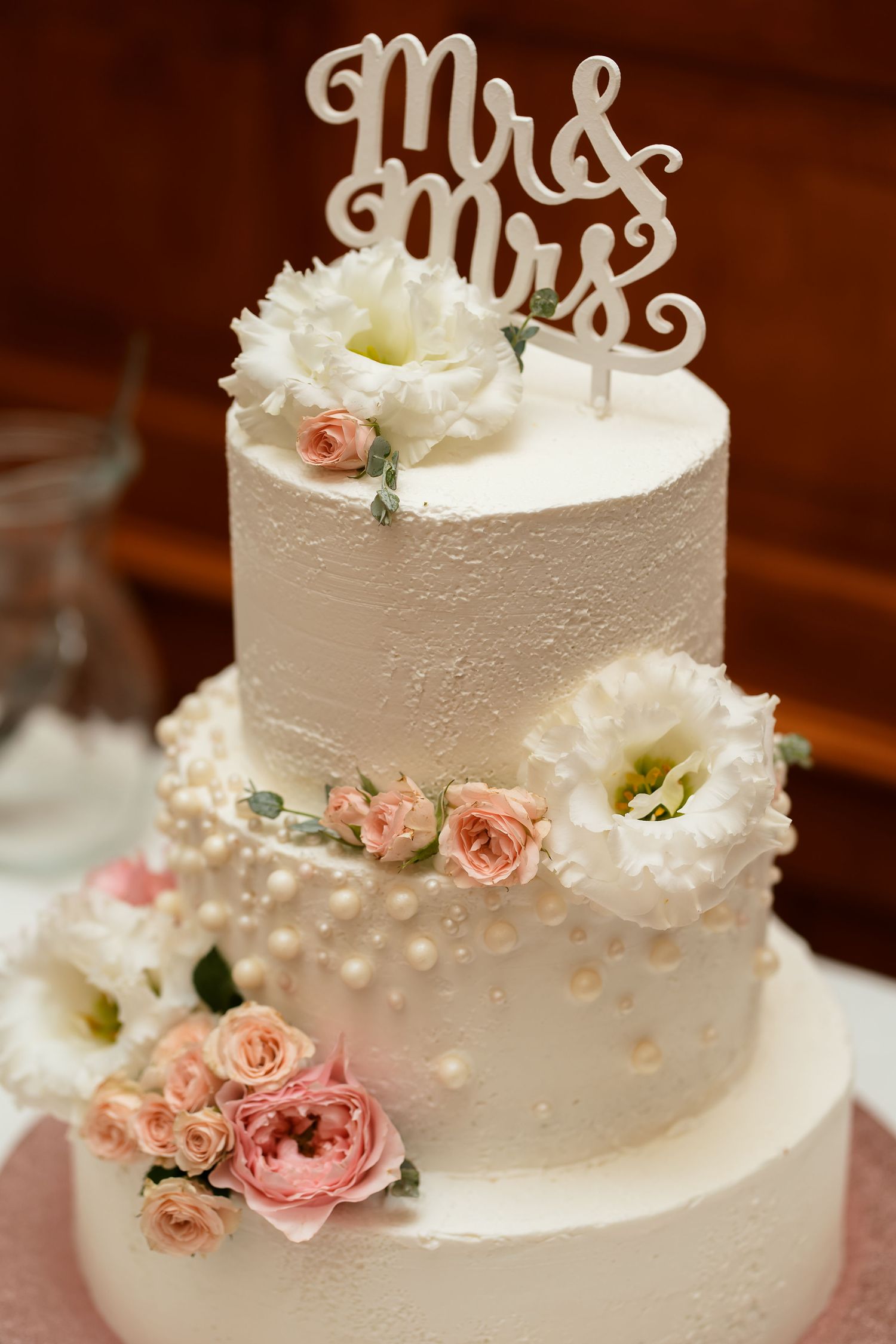 Three-tiered white wedding cake with Mr & Mrs topper and blush roses.