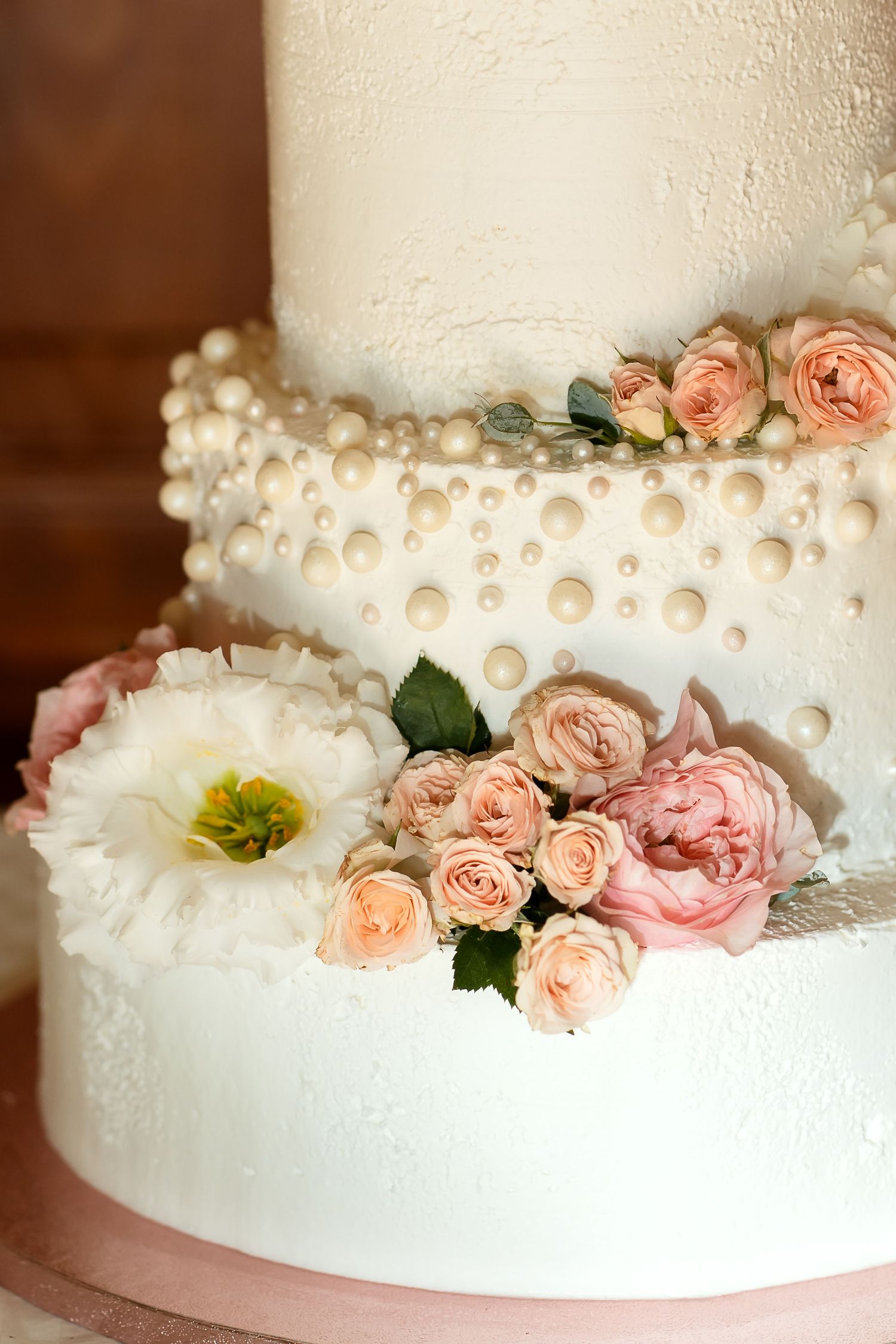 Elegant white wedding cake decorated with pearls and peach roses.