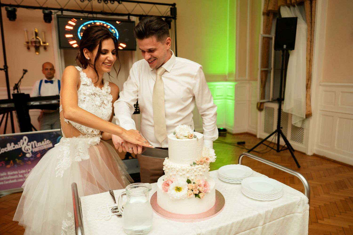 Newlyweds working together to cut their white and pink wedding cake at reception.