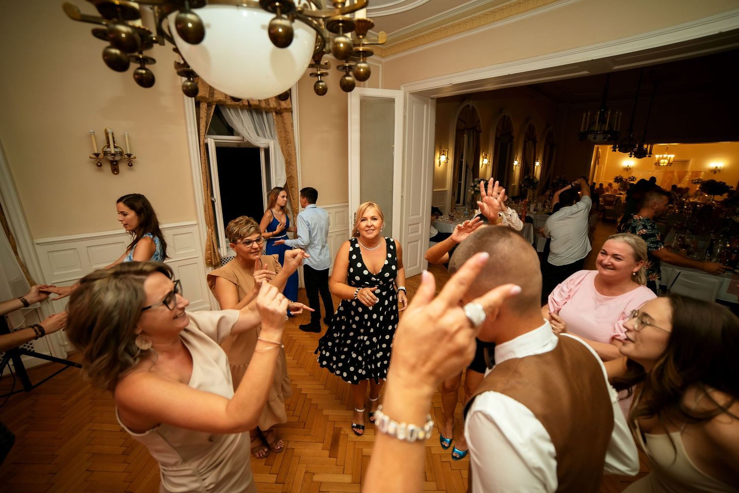 Wedding guests dancing and celebrating on parquet floor with ambient green lighting.