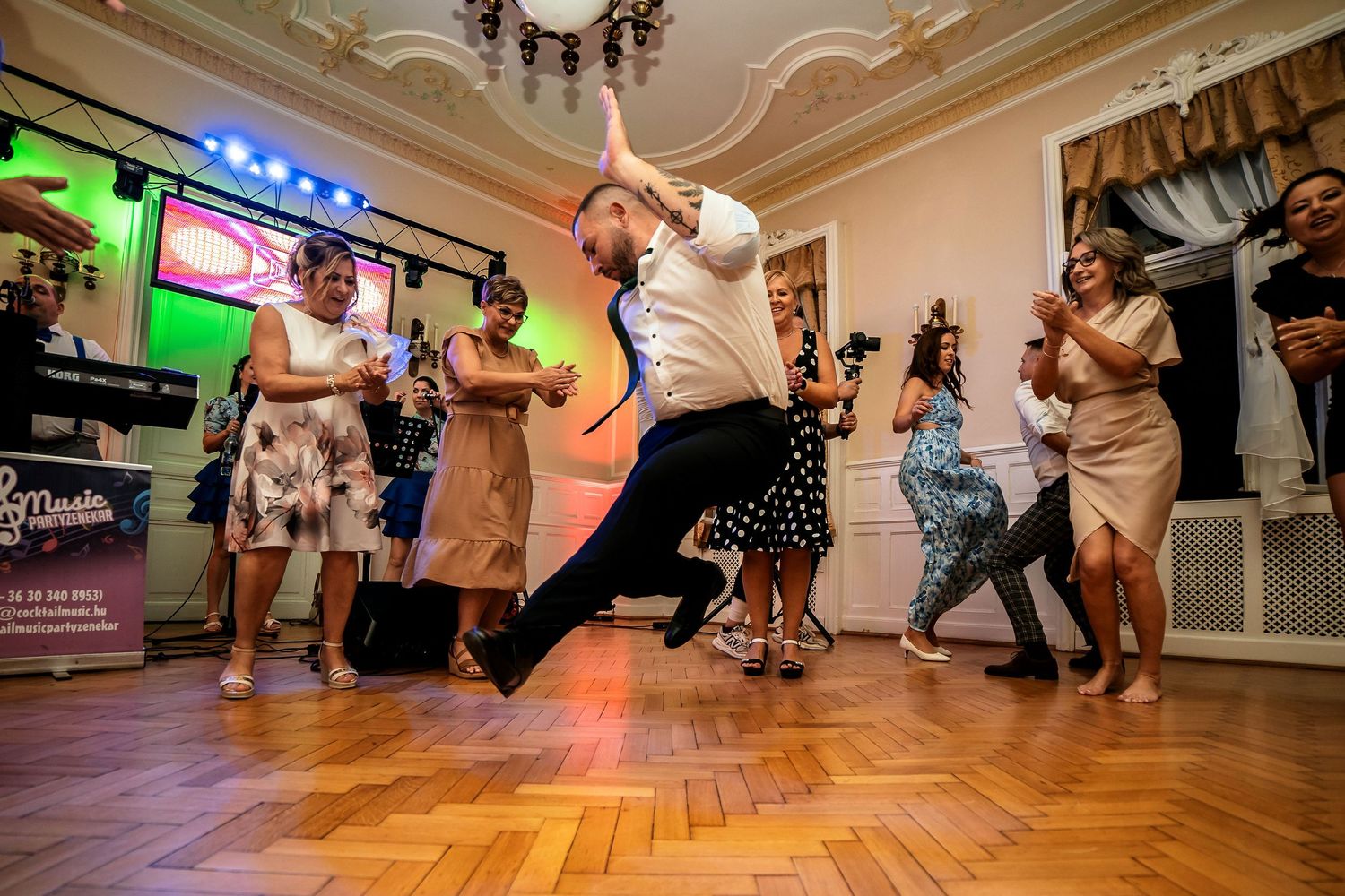 People dancing enthusiastically on a wooden floor with colorful party lighting.