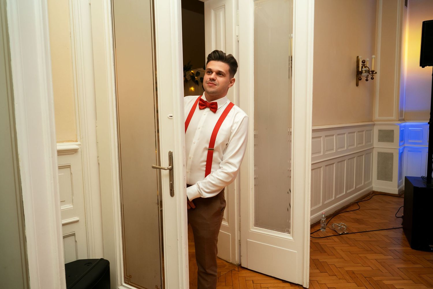 Person in formal attire posing in an elegant hallway with wainscoting and white doors.