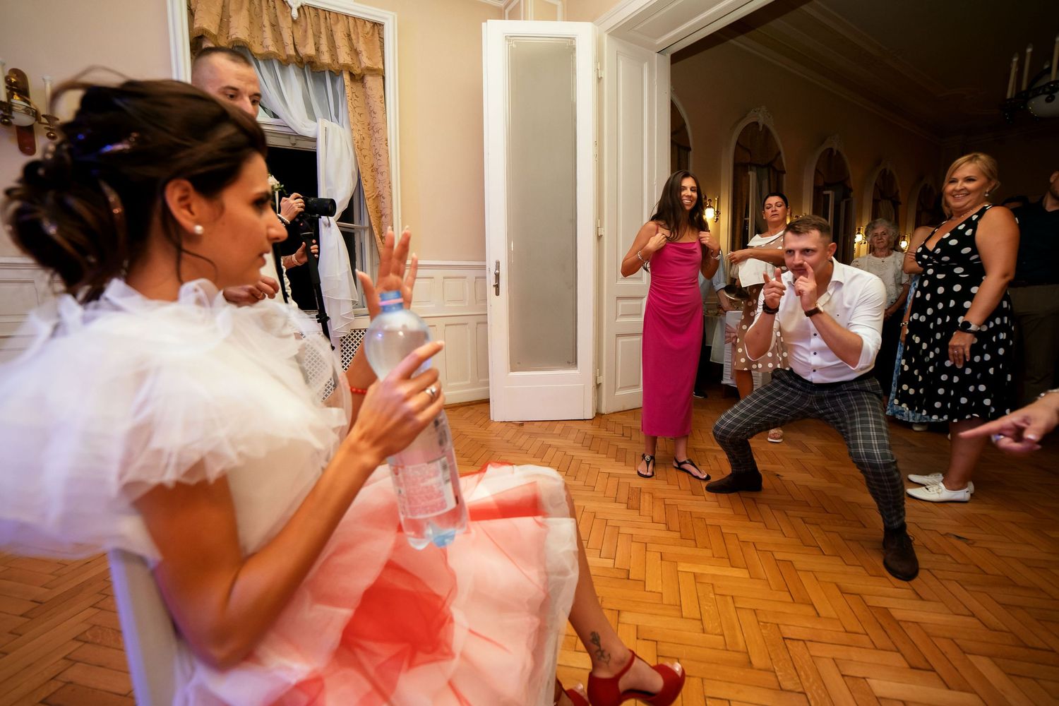 Lively party scene with attendees dancing and socializing on a herringbone wood floor.